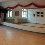 Tanzstudio mit Laminatboden, Spiegelwand, großen Fenstern und Palme.