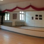 Tanzstudio mit Laminatboden, Spiegelwand, großen Fenstern und Palme.