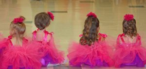 Stundenplan: Kleine Tänzerinnen von hinten, die im Tutu auf dem Boden sitzen.